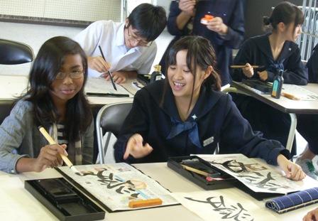 半紙に筆で「愛」という漢字を書いたインターナショナルスクールの生徒と隣でその文字を指さしている女子生徒の写真