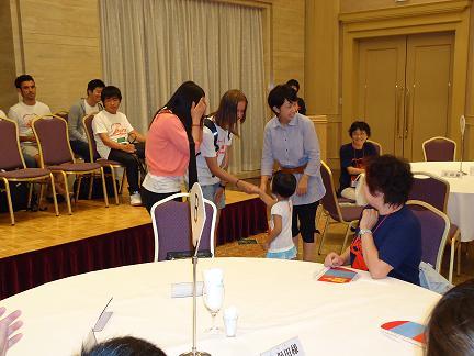 会場で小さな女の子と留学生が握手をしている写真