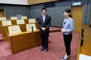 アナウンサーと議員の二人が議会室に立っている画像