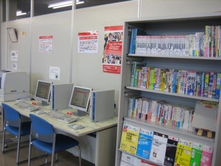 2台のパソコンとその奥にプリンター、たくさんの本が並んでいる本棚の写真