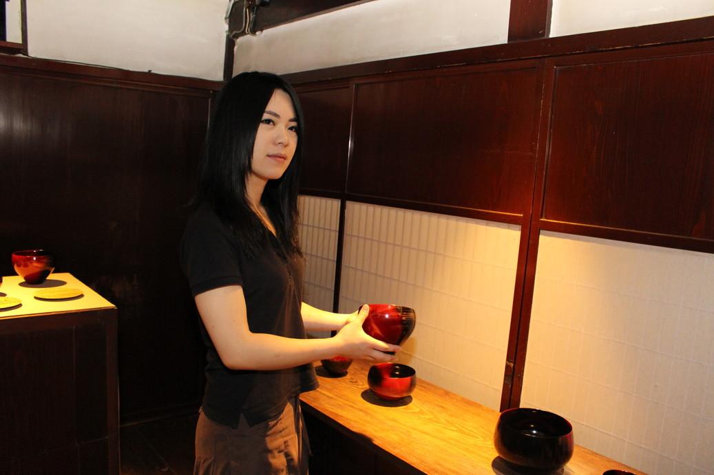 工房に展示されている赤いお椀を手に持っている田中さんの写真
