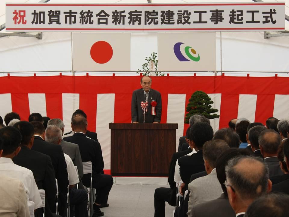 紅白の幕の前で、聴衆に向かって話をしている男性の写真